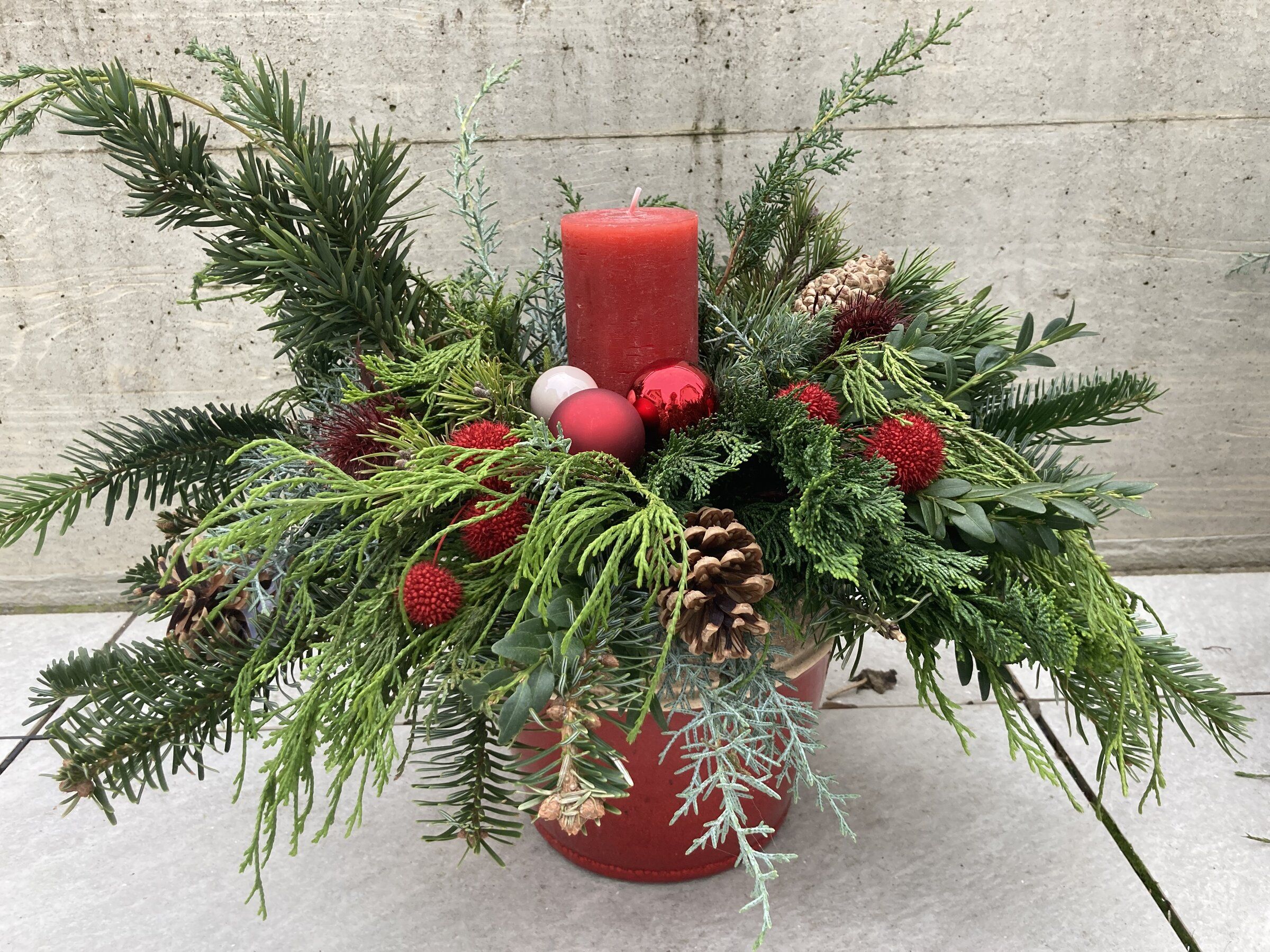 Adventsgesteck mit roter Kerze, Tannenzweigen, Zapfen und roten Beeren