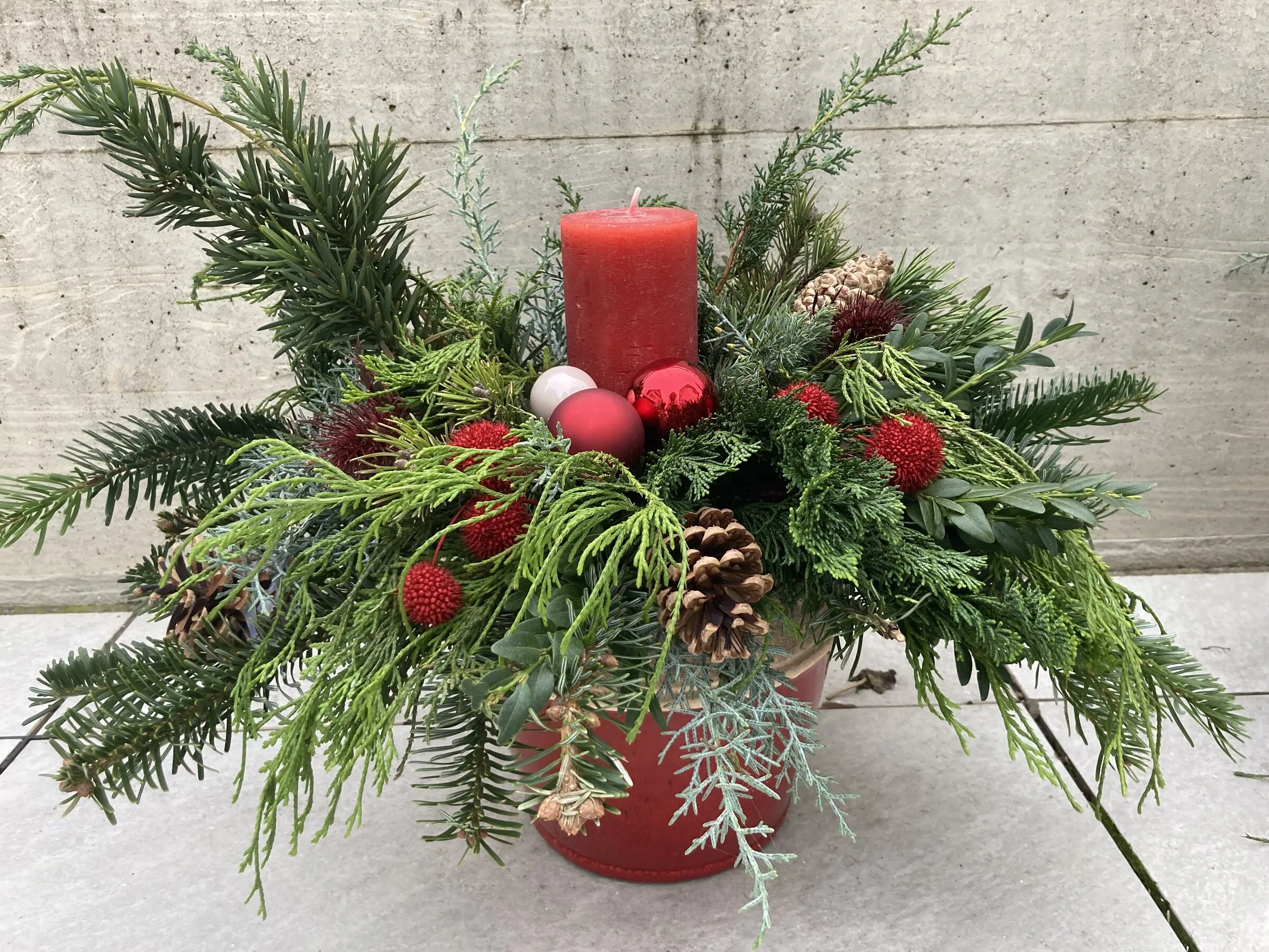 Adventsgesteck mit roter Kerze, Tannenzweigen, Zapfen und roten Beeren