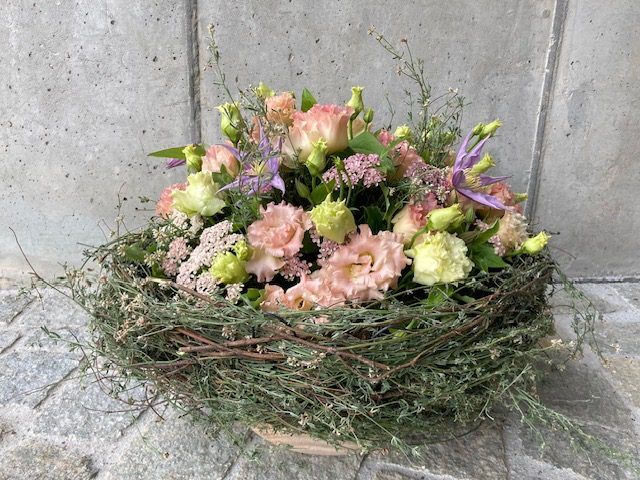 Frühlingshaftes Blumengesteck in Weidenkorb mit Rosen und Lisianthus