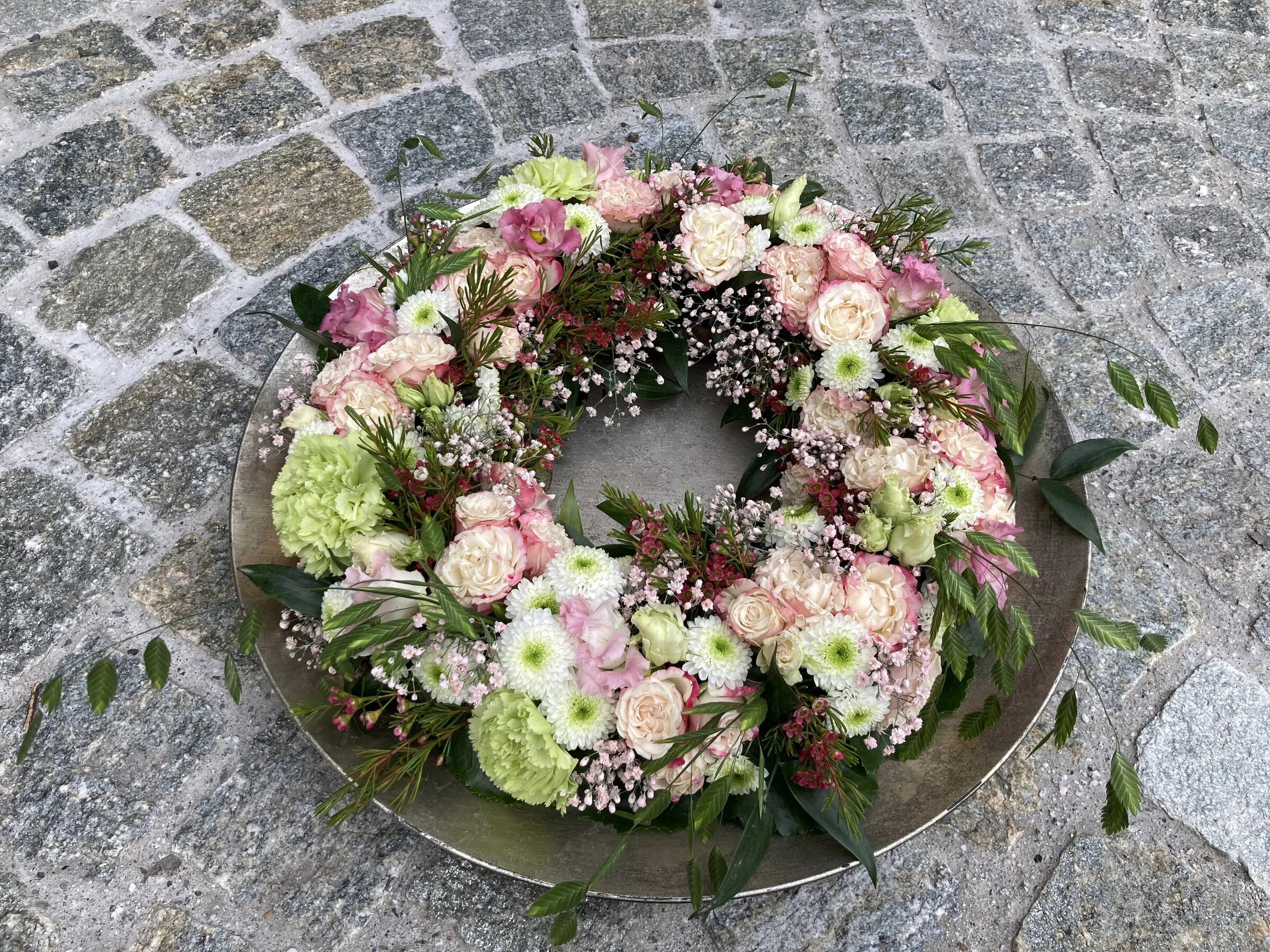 Blumenkranz in Rosa und Grün mit Rosen und Chrysanthemen auf Metallschale
