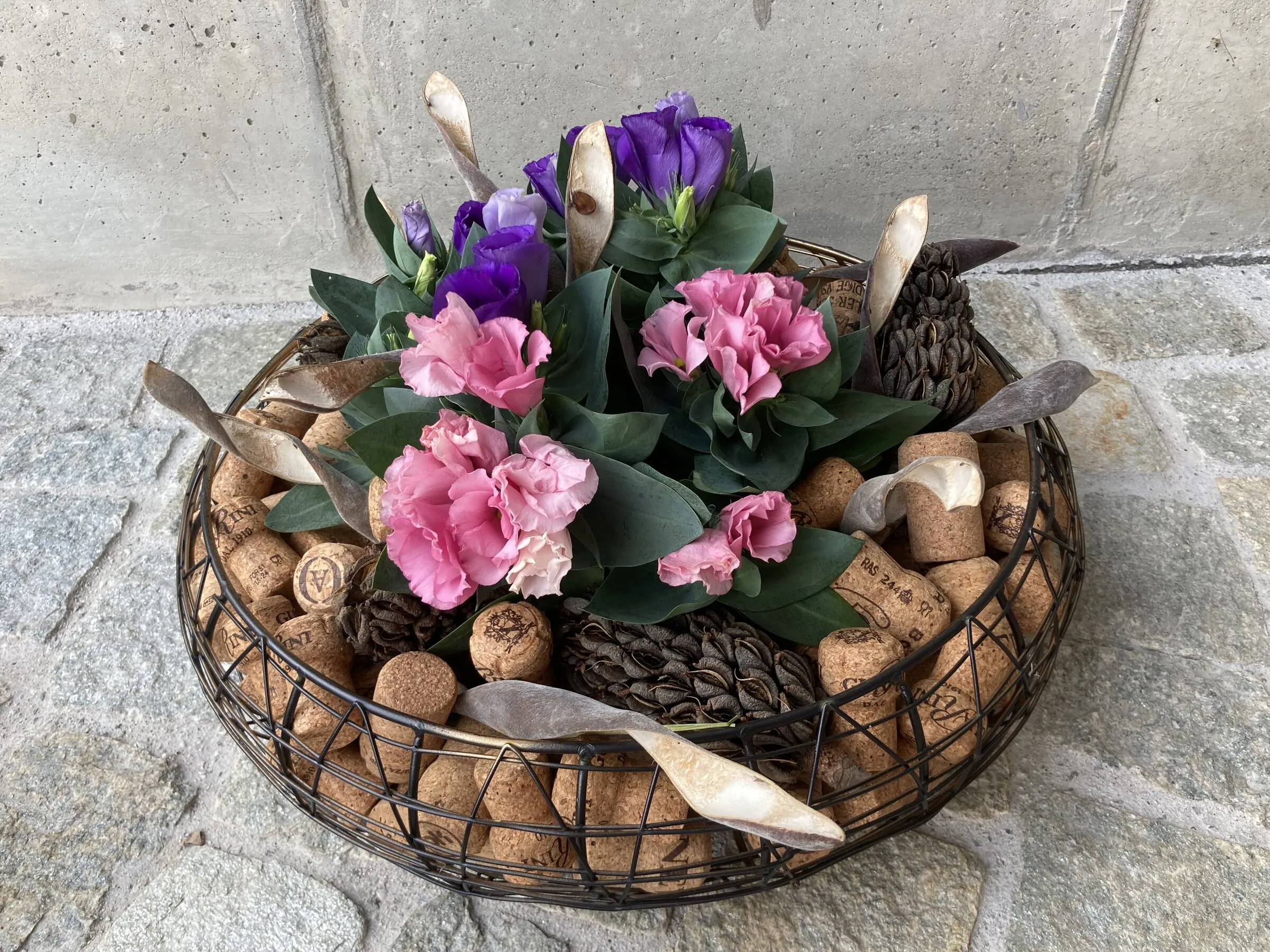 Gesteck im Drahtkorb mit Korken, pinken Nelken und violettem Lisianthus
