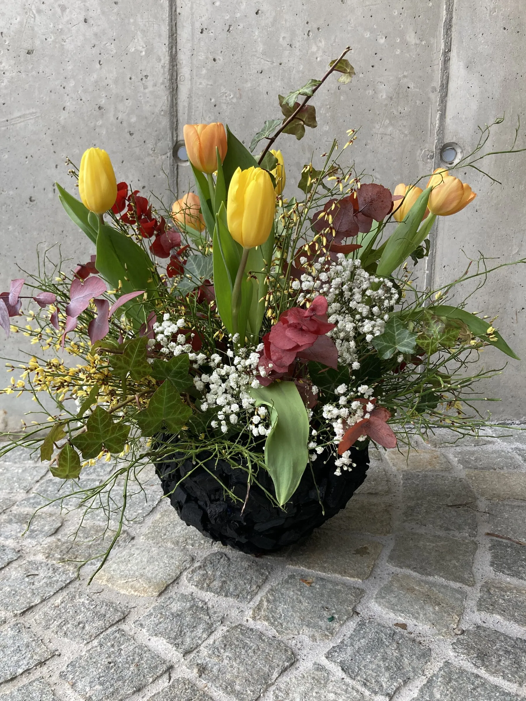 Frühlingsgesteck mit gelben Tulpen, Orchidee und Mimosen in dunkler Schale