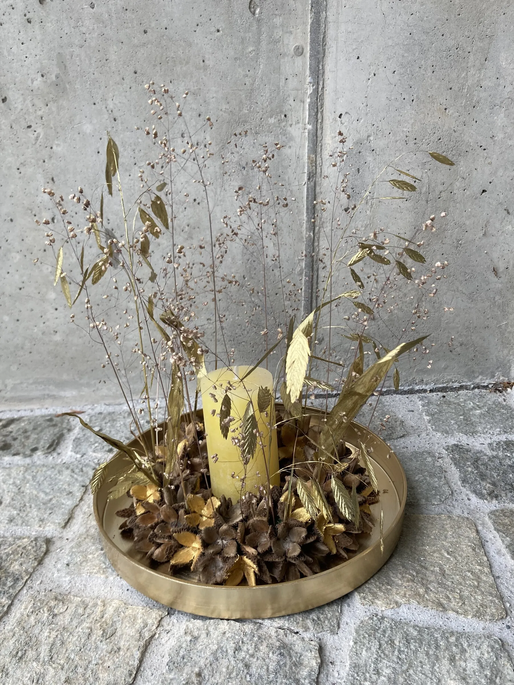 Goldene Schale mit Kerze, Trockengräsern und vergoldeten Blättern