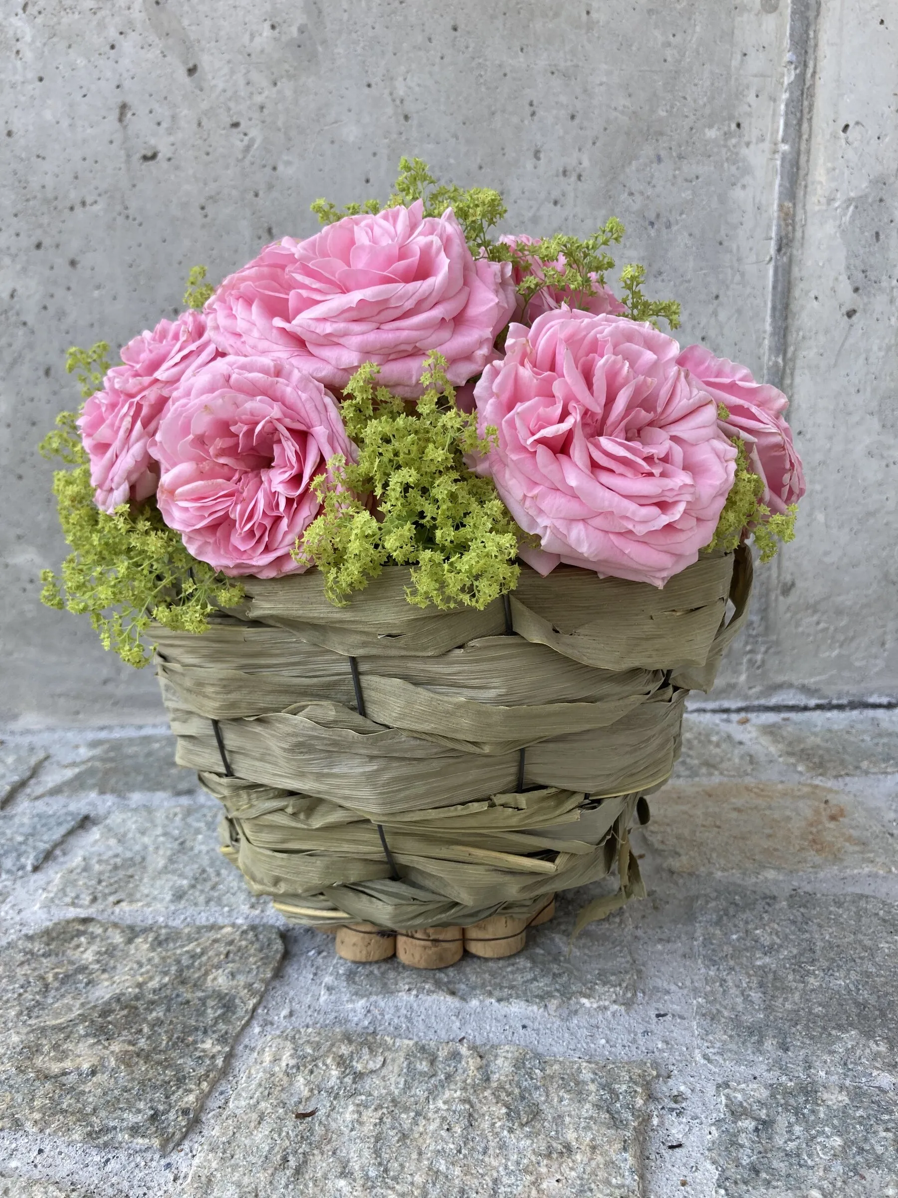 Geflochtener Graskorb mit rosa Gartenrosen und Frauenmantel