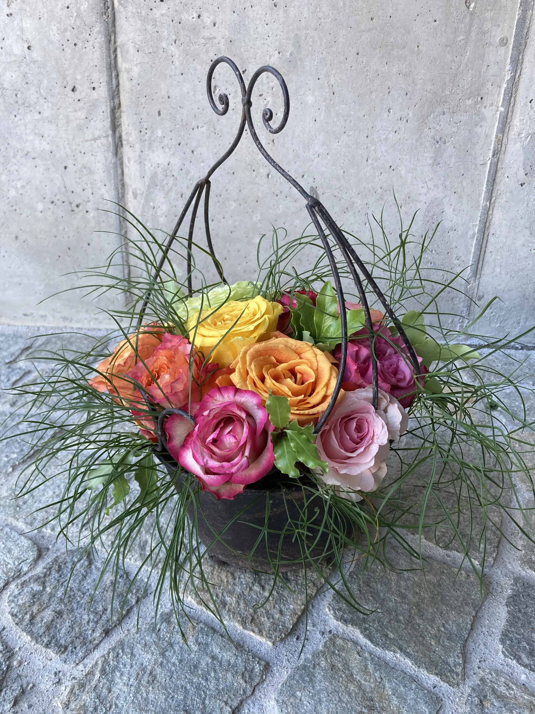 Gesteck in Schale mit geschwungenem Henkel, orange und pinke Rosen mit Gräsern