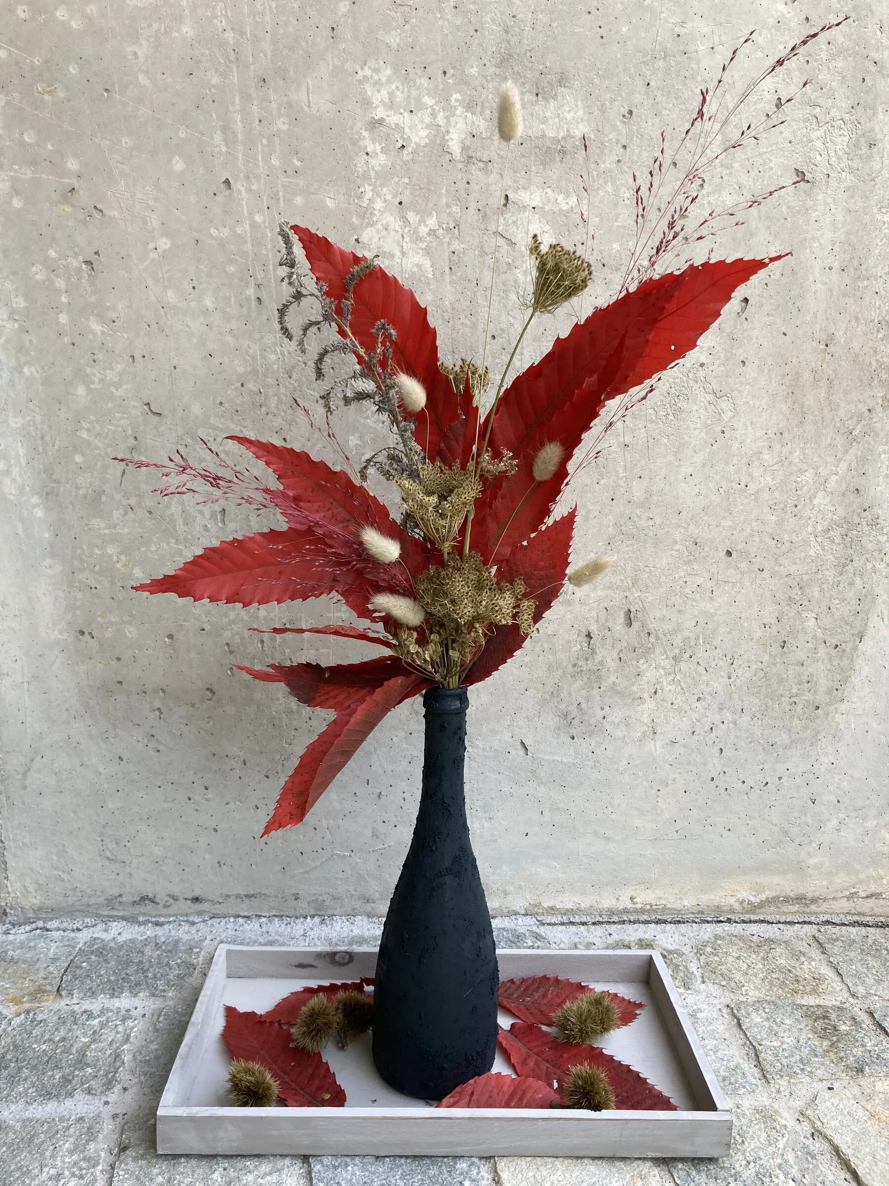 Herbstgesteck mit roten Blättern und Trockengräsern in schwarzer Vase
