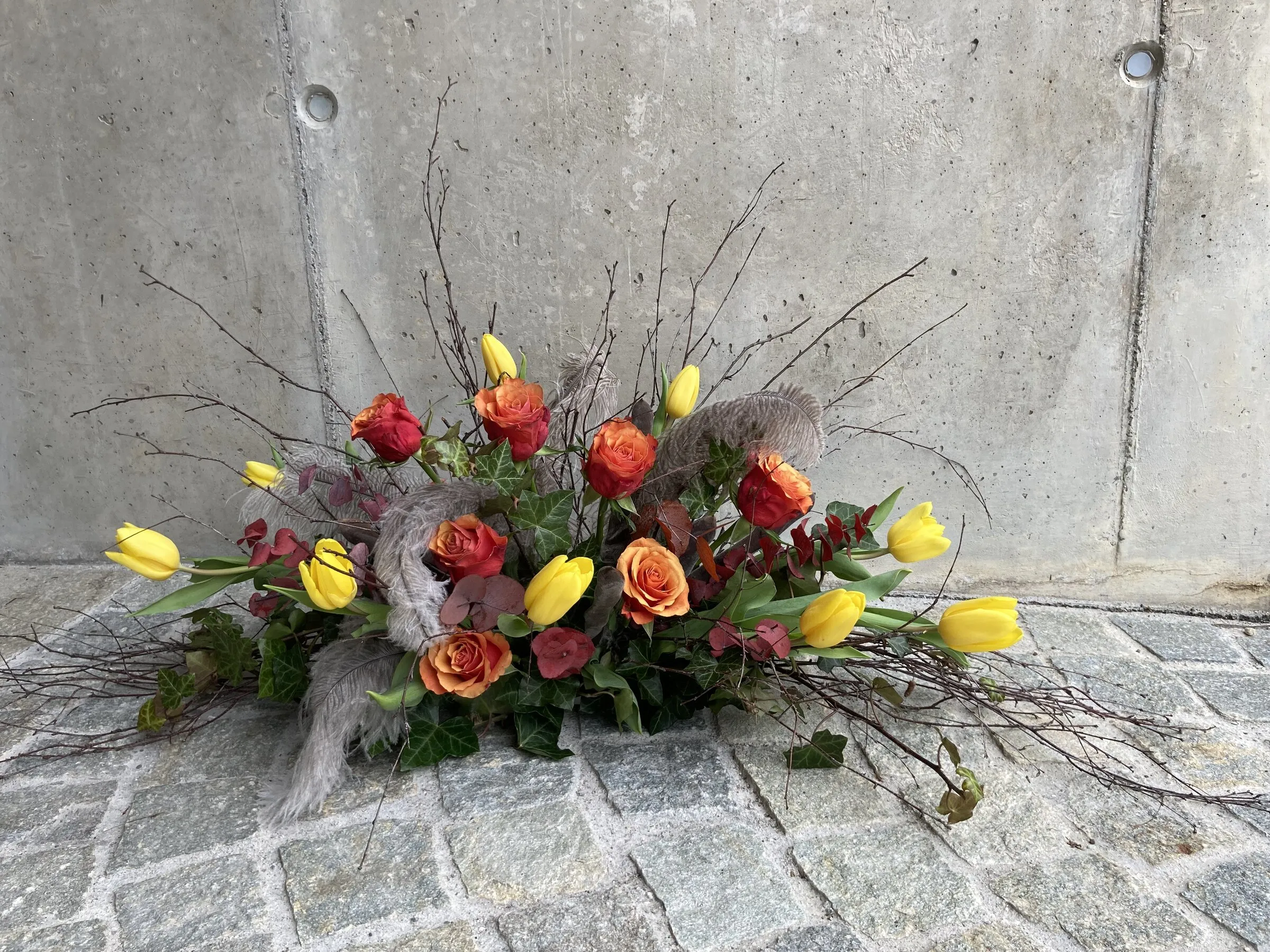 Längliches Frühlingsgesteck mit gelben Tulpen, orangen Rosen und Zweigen
