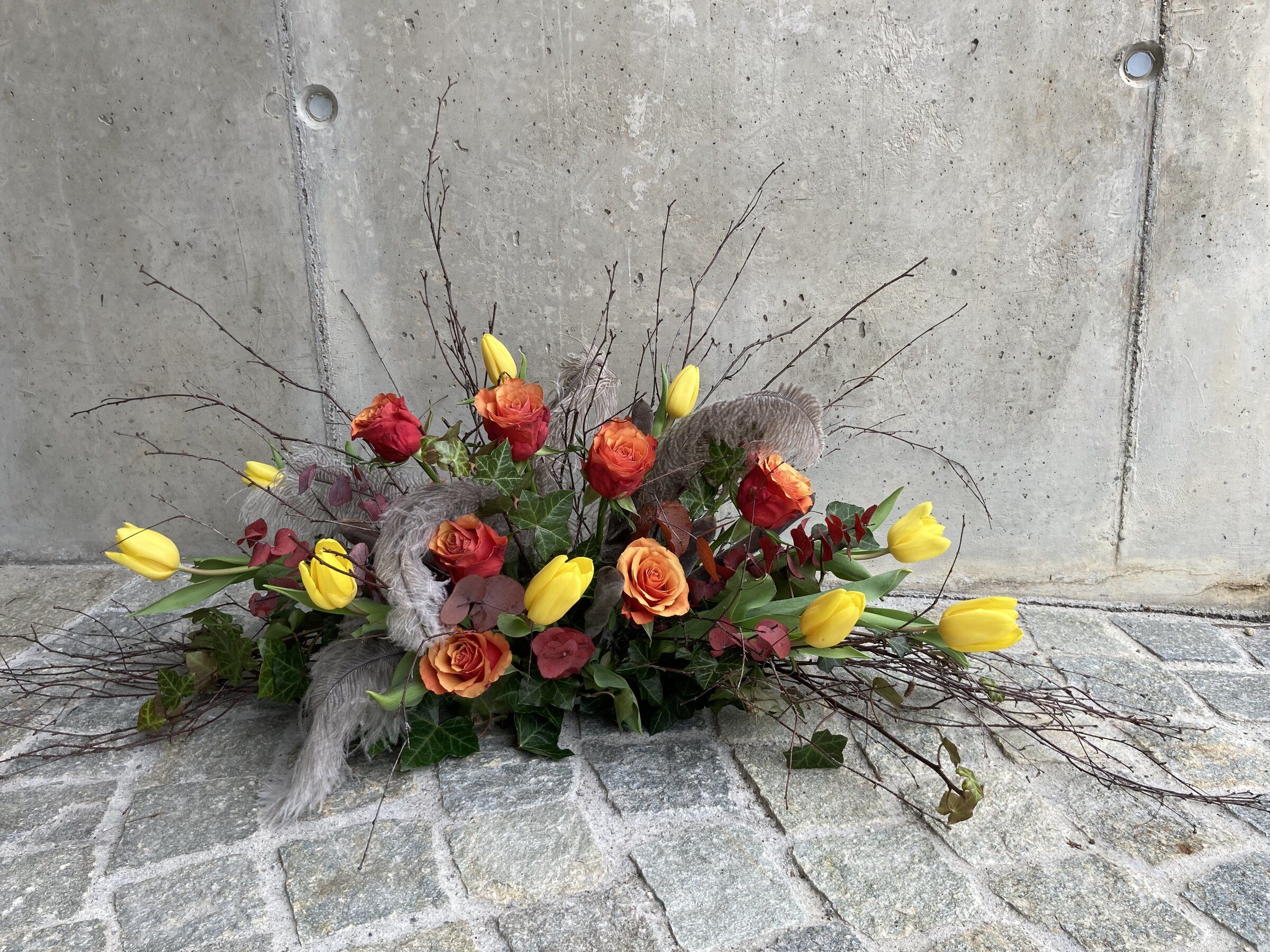 Längliches Frühlingsgesteck mit gelben Tulpen, orangen Rosen und Zweigen