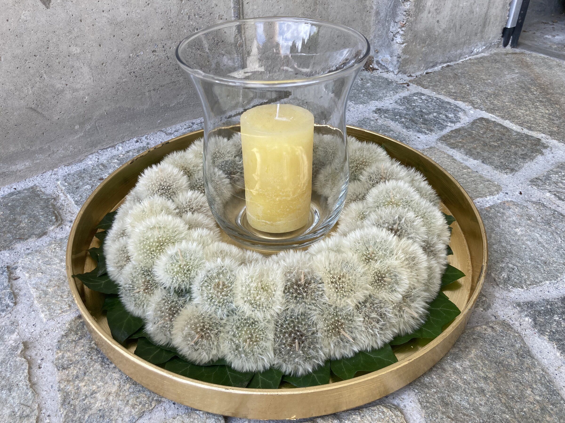 Kranz aus Pusteblumen auf goldenem Tablett mit Windlicht