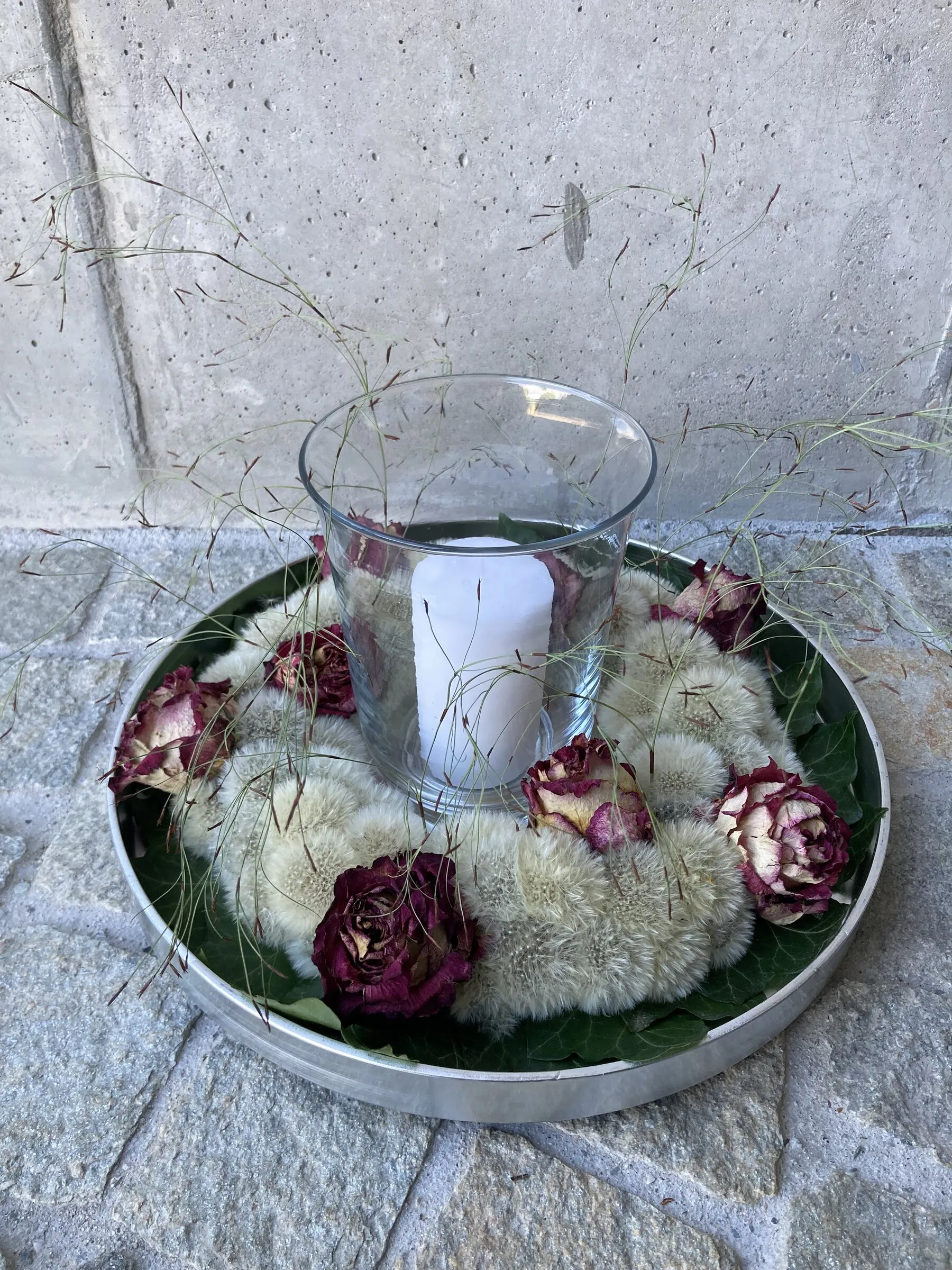 Pusteblumenkranz mit getrockneten dunkelroten Rosen und Windlicht auf Silbertablett