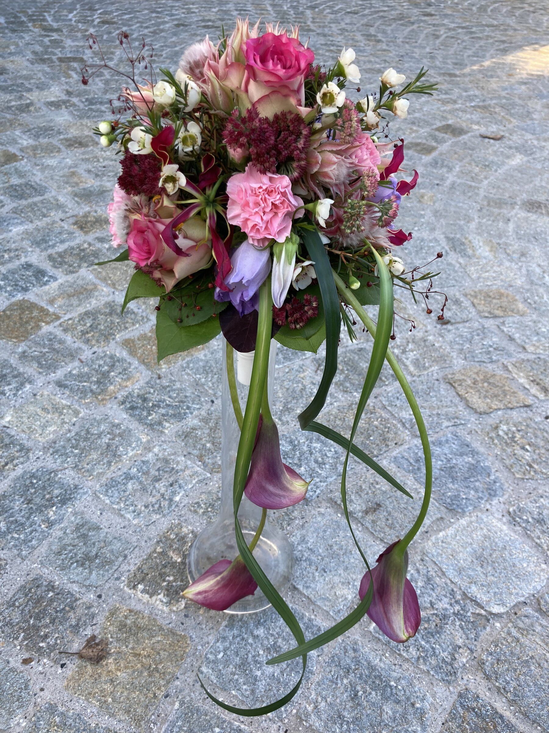 Pinkfarbener Strauss mit über die Glasvase fallenden Callas