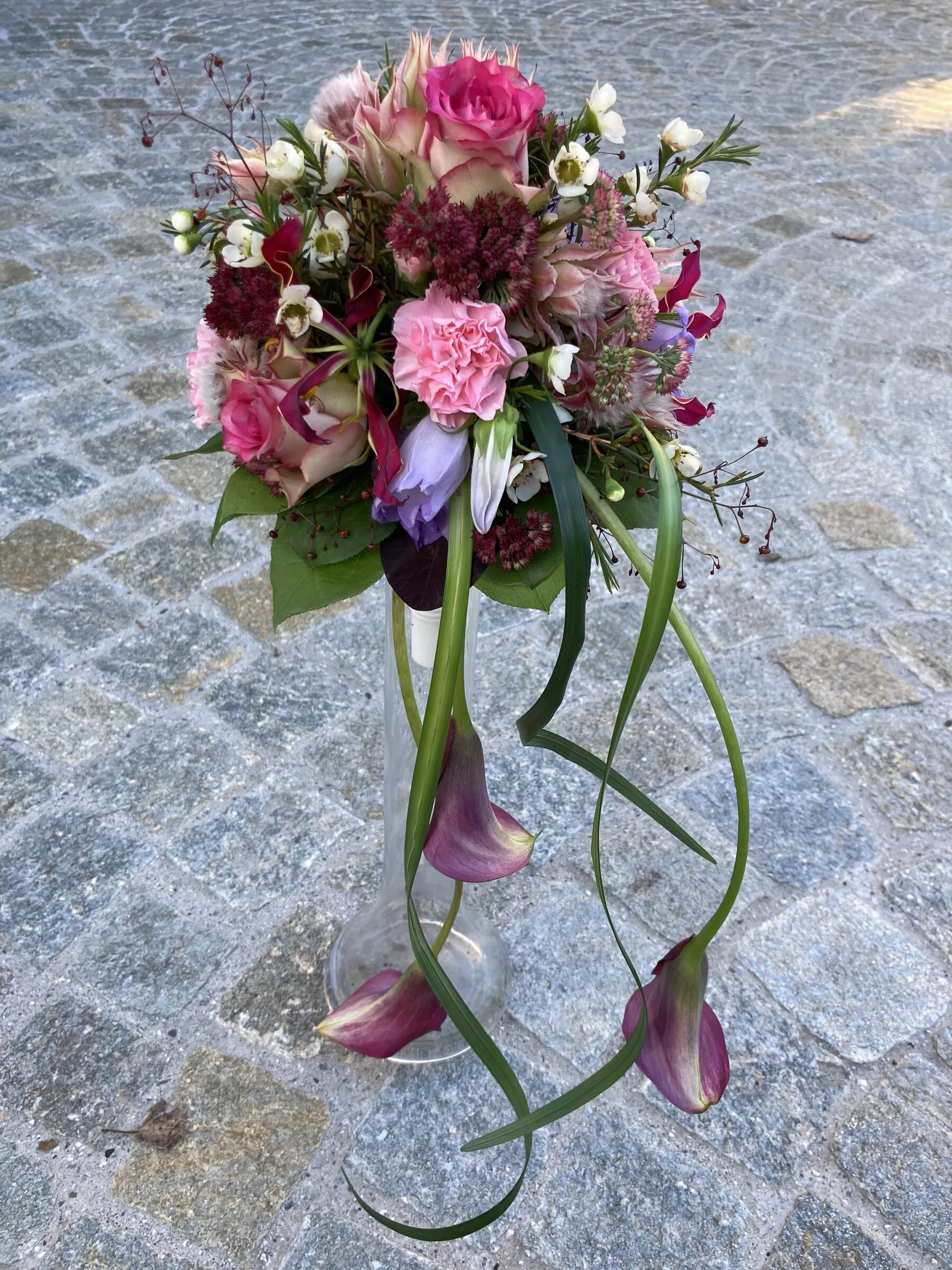 Pinkfarbener Strauss mit über die Glasvase fallenden Callas