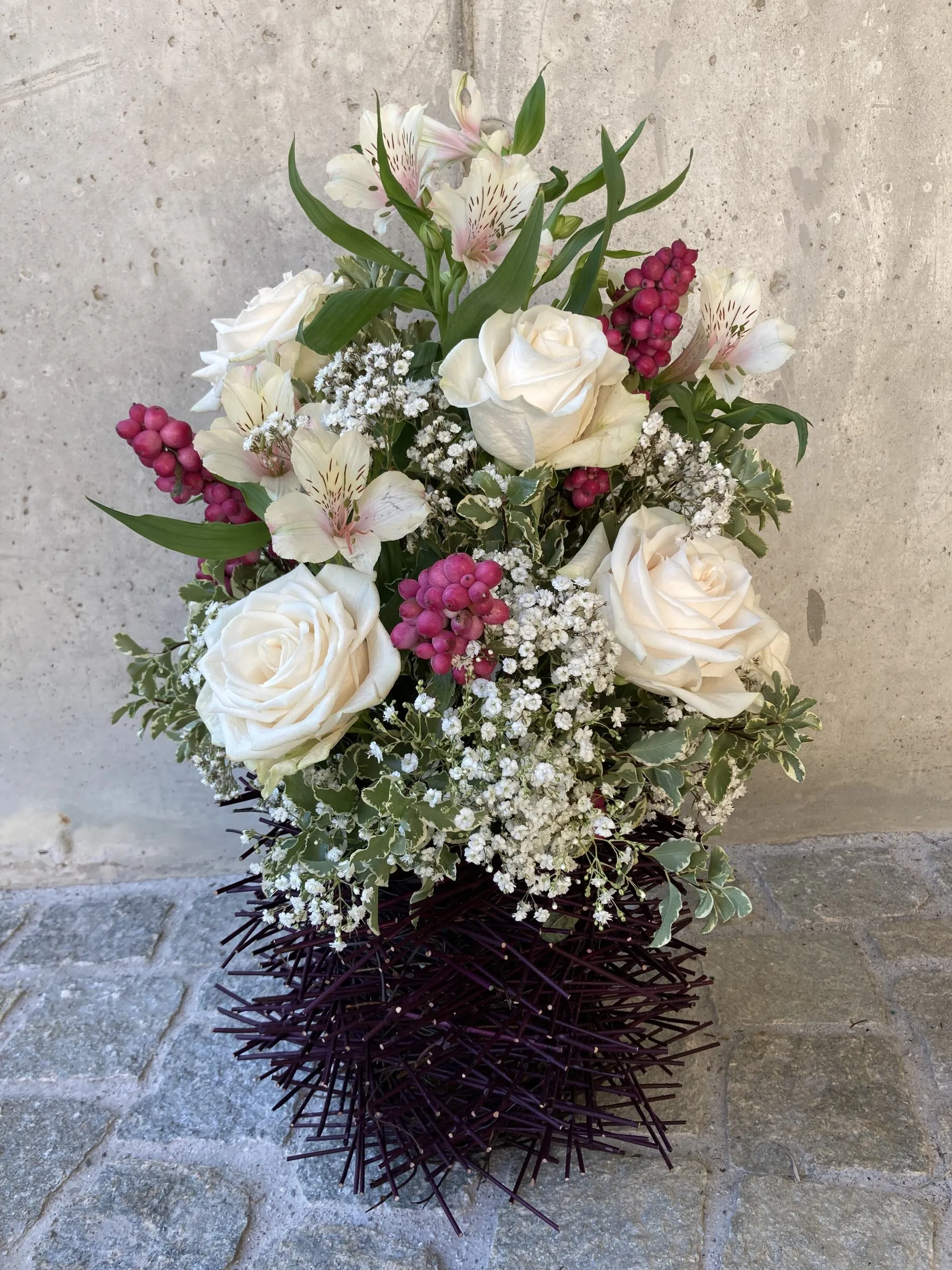 Strauss mit weissen Rosen, pinken Beeren und Schleierkraut auf dunkler Dornenvase