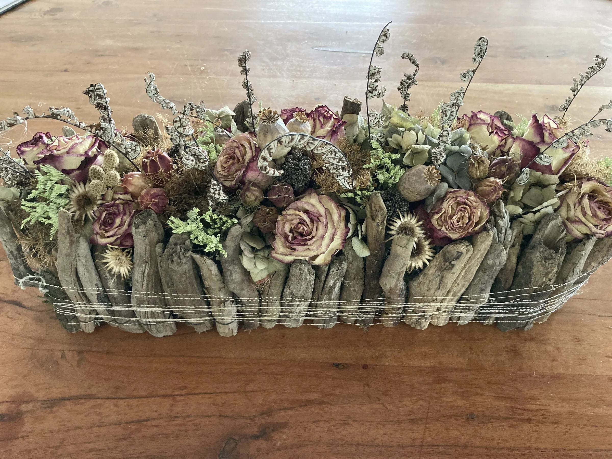 Trockengesteck in Holzschale mit getrockneten Rosen und Strohblumen